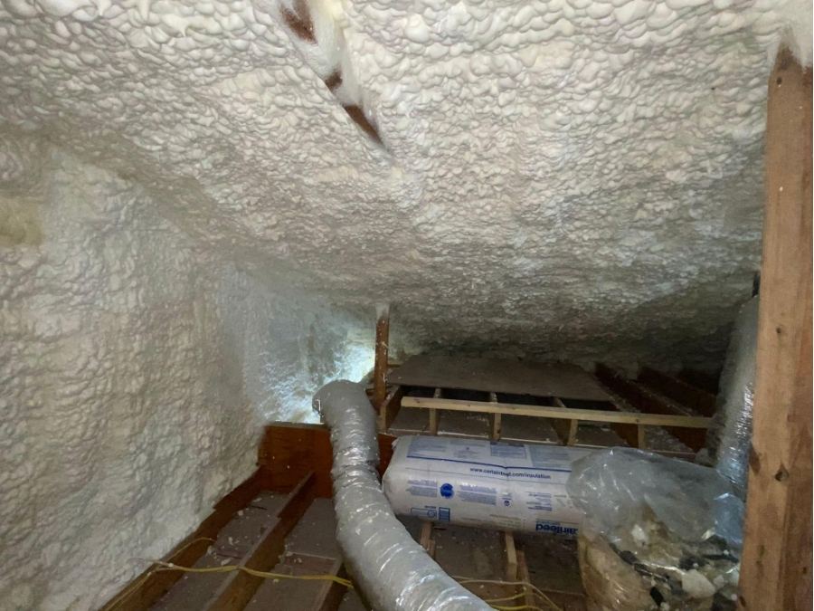 Attic spray foam insulation upgrade showing thick coverage on roof rafters and walls near HVAC ducting for better home climate control