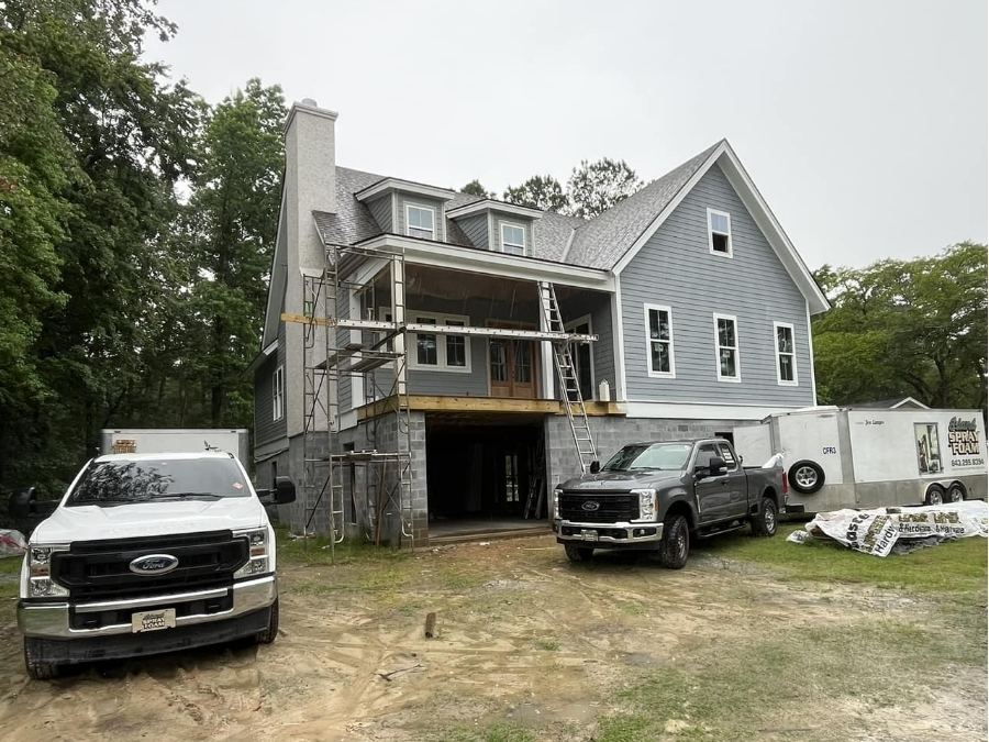 Island Spray Foam trucks and equipment on-site at a new residential construction project in Bluffton, SC, featuring a gray two-story home under development.