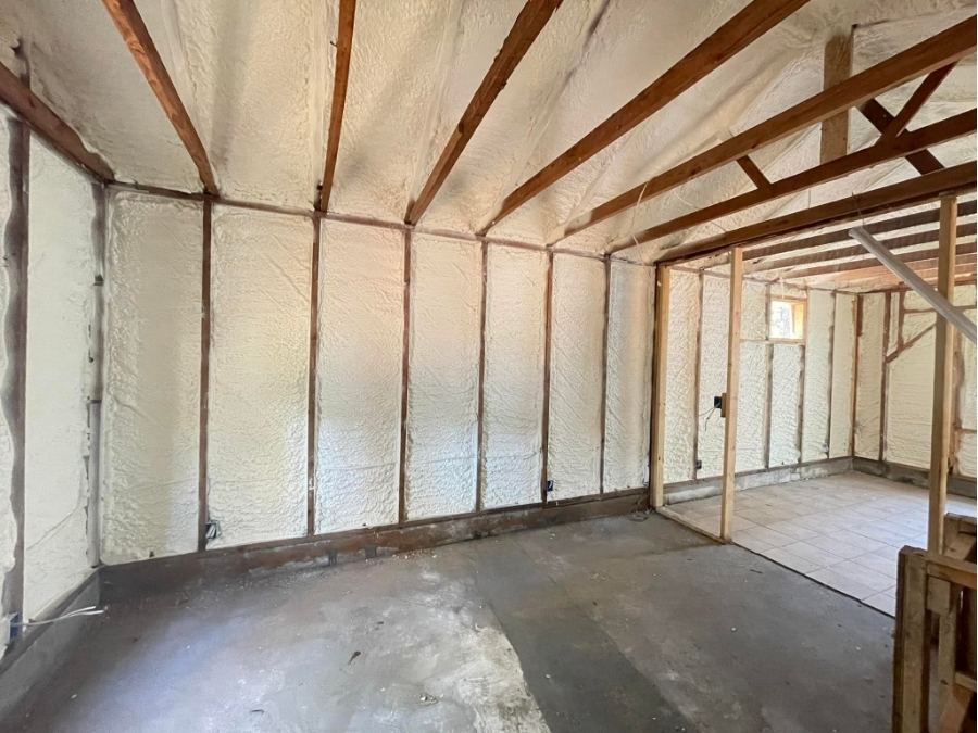 Interior view of a residential garage or shed with fresh spray foam insulation applied between wooden wall studs and ceiling rafters for energy efficiency